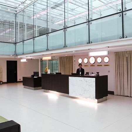 Dubai International Terminal Hotel Exterior photo The photo depicts a modern hotel lobby with a sleek and minimalist design. There is a reception desk made of dark wood and marble, situated in the center of the lobby. A staff member is standing behind the desk, attending to guests. The lobby feature