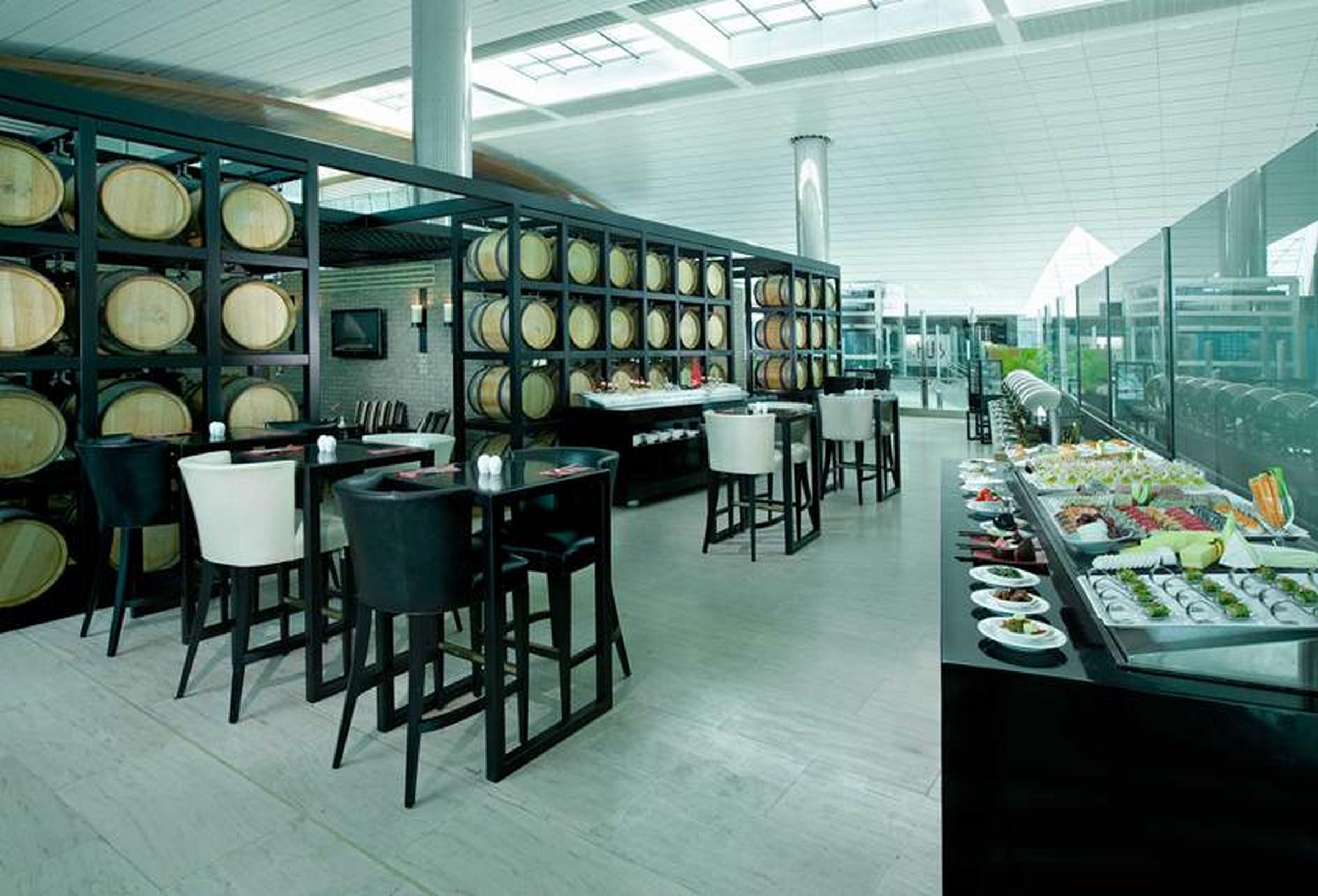 Dubai International Terminal Hotel Exterior photo The photo depicts a modern, stylish restaurant interior. There are tall tables and high-backed chairs arranged in the dining area, with some featuring a black and white color scheme. Behind the tables, there are large shelves or racks displaying wine