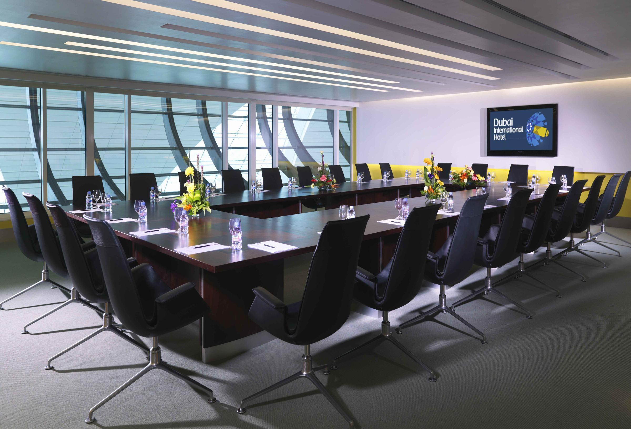 Dubai International Terminal Hotel Business photo The photo depicts a modern conference room. It features a long, rectangular wooden table surrounded by black ergonomic chairs. The room is well-lit with large windows that allow natural light to filter in, creating a bright atmosphere. There are deco