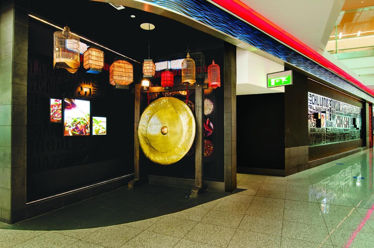 Dubai International Terminal Hotel Exterior photo The photo shows an entrance to a restaurant or dining area decorated with Asian-inspired elements. There are colorful lanterns hanging from the ceiling, adding a warm ambiance. A large gong is prominently displayed on a stand, suggesting a theme rela