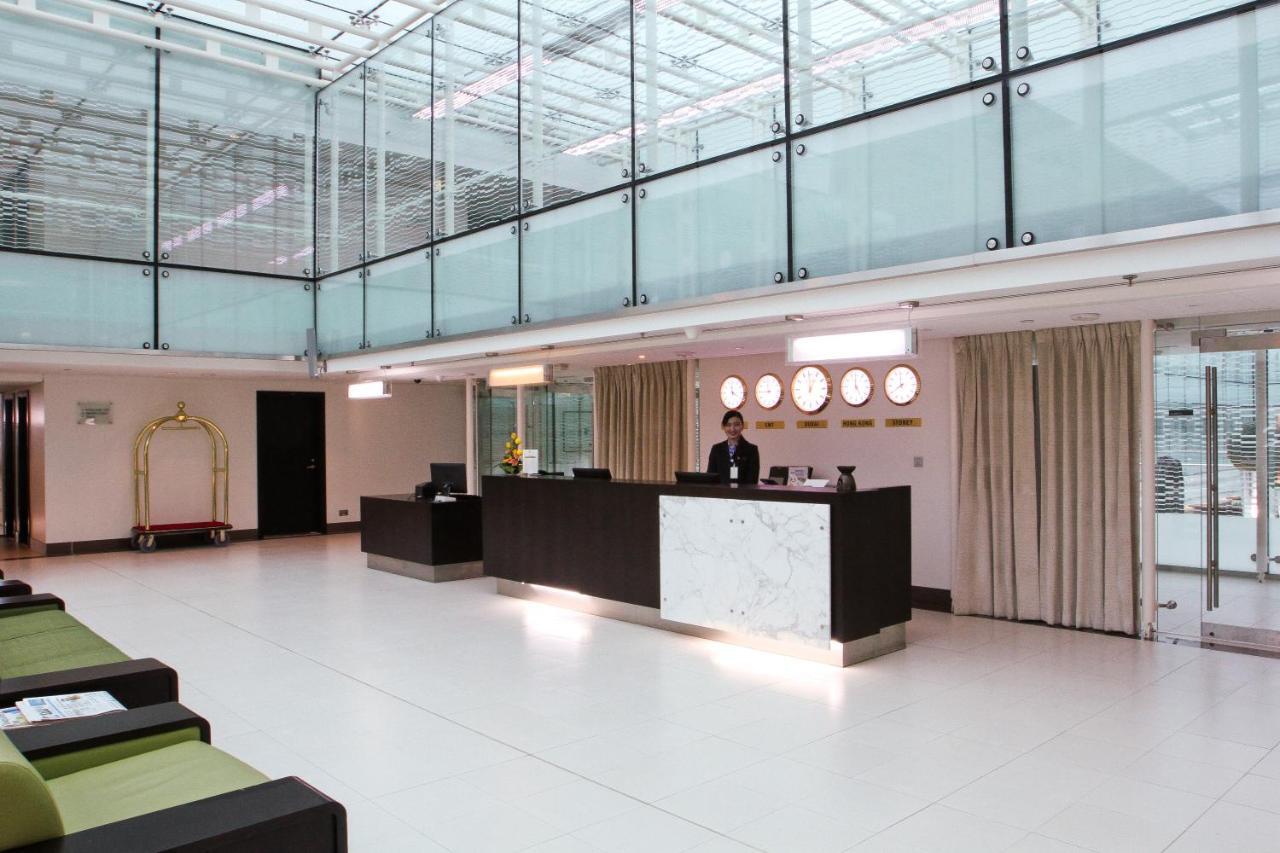 Dubai International Terminal Hotel Exterior photo The photo depicts a modern hotel lobby with a sleek and minimalist design. There is a reception desk made of dark wood and marble, situated in the center of the lobby. A staff member is standing behind the desk, attending to guests. The lobby feature