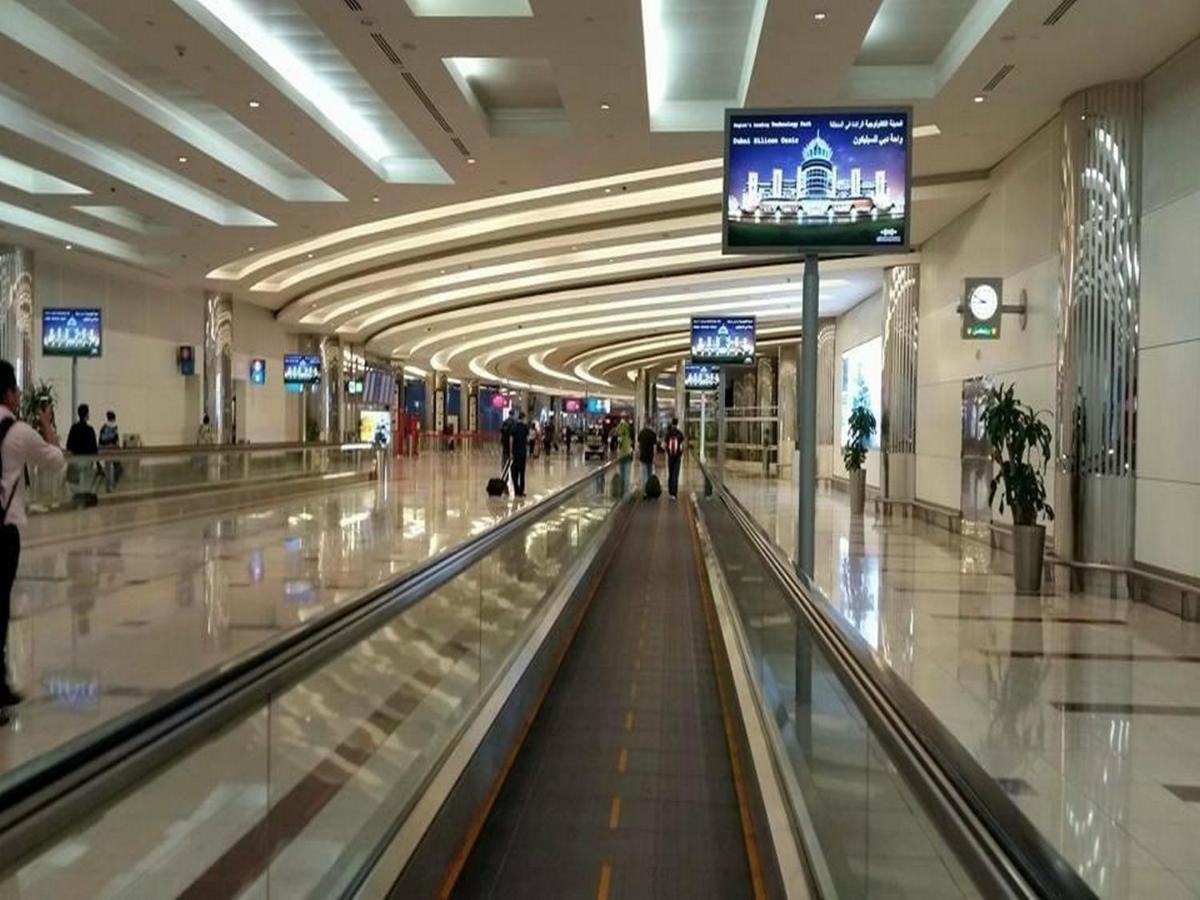 Dubai International Terminal Hotel Exterior photo The photo shows an airport interior with a modern and spacious design. There is a long moving walkway in the center, flanked by various shops and terminals. The ceiling features elegant lighting and a smooth, curved structure, creating a welcoming at