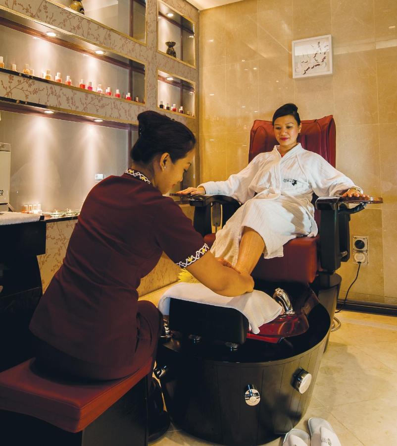 Dubai International Terminal Hotel Exterior photo The photo depicts a spa or wellness setting where a woman is receiving a foot massage or pedicure. She is seated comfortably in a plush chair, wearing a white robe. A technician, dressed in a maroon uniform, is attending to her feet, likely performin