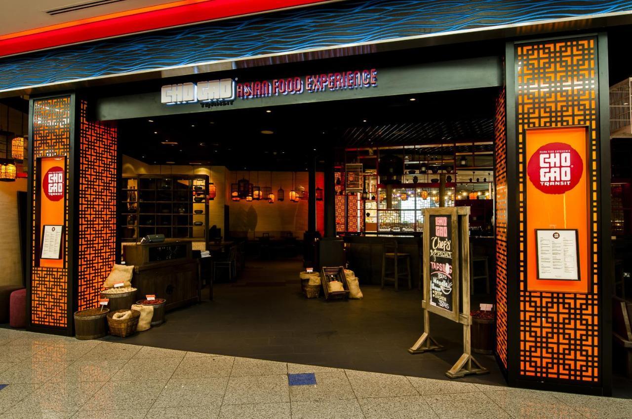 Dubai International Terminal Hotel Exterior photo The photo shows the entrance to a restaurant called "Cho Gao," which is described as a "Vietnamese Food Experience." The exterior features a modern design with colorful decorations. There are warm lighting and an inviting atmosphere visible through t